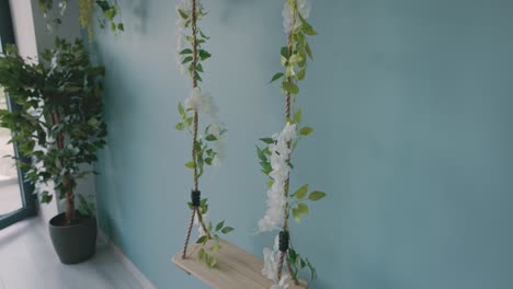 a wooden swing hanging against the wall of a beauty salon, embellished with artificial leaves and flowers