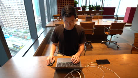 timelapse, chinese asian millennial with glasses sitting in front of laptop, working in empty co-working space