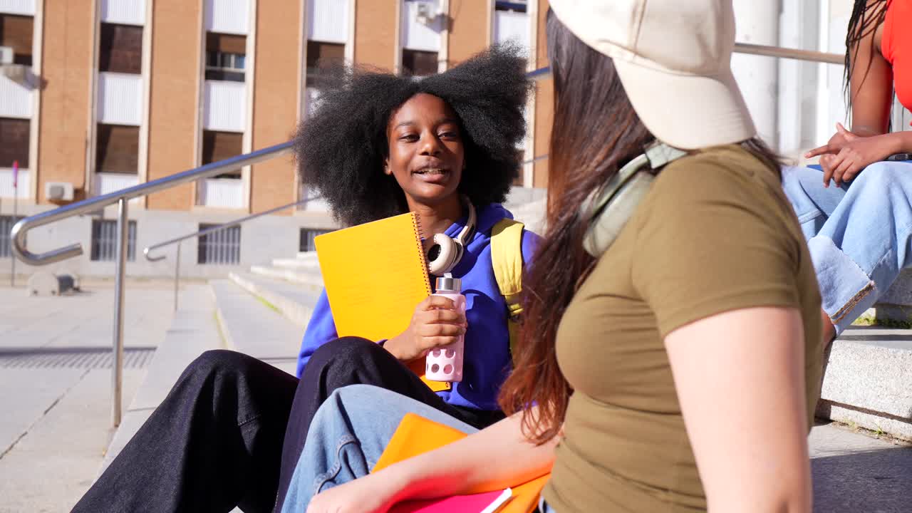 Giovane studentessa di colore che parla con un amico sui gradini del campus universitario