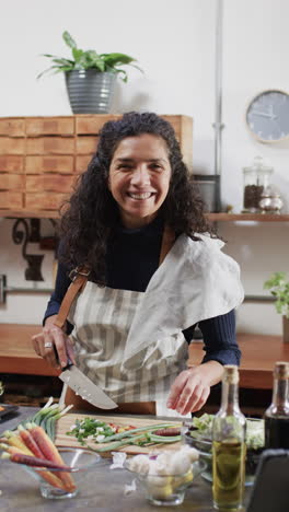 vertical video of portrait of happy biracial woman chopping vegetables in kitchen, slow motion