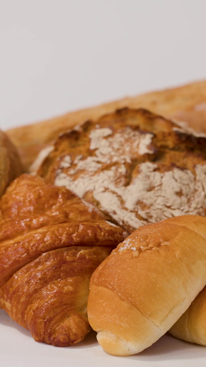 Ripresa panoramica ravvicinata di mani che dispongono vari tipi di pane artigianale, croissant e pagnotte di pane a lievitazione naturale affettate