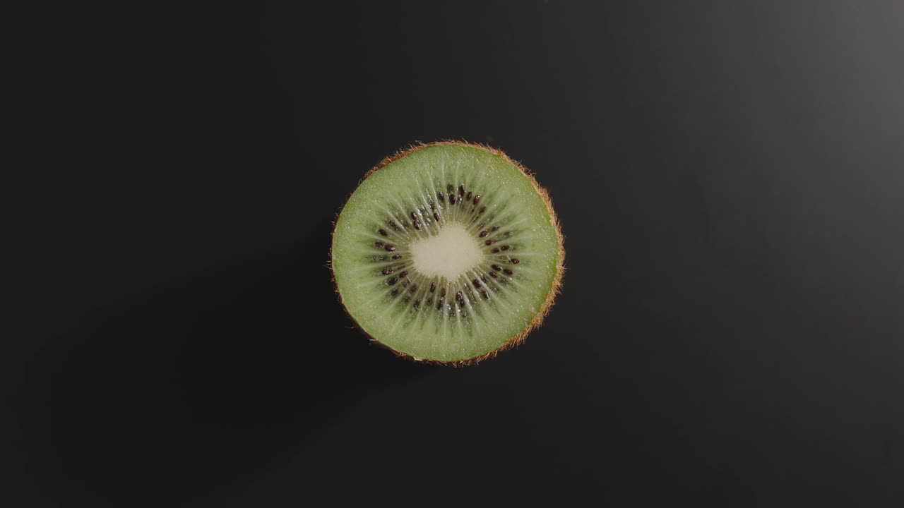 Half of a kiwi rotates on a black surface. Top view. Stop motion