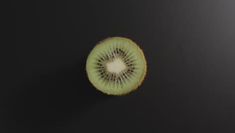 la mitad de un kiwi gira sobre una superficie negra. vista de arriba. detener el movimiento