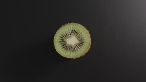 half of a kiwi rotates on a black surface. top view. stop motion