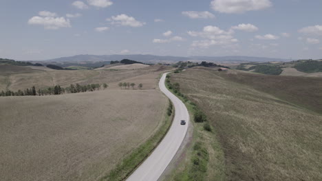 drone shot of winding roads and golden farm fields in tuscany italy landscape on a sunny day with blue sky and clouds on the horizon log