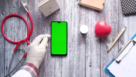 vista superior de la mano del médico en guantes usando un teléfono inteligente con pantalla verde