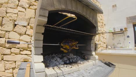 pollo asado girando en una barbacoa de ladrillos refractarios de madera y carbón asado a fuego lento