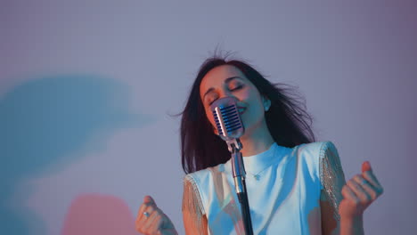 cantante en un vestido blanco actuando apasionadamente, manos juntas y ojos cerrados, expresando una profunda emoción. su cabello fluye contra un suave fondo de gradiente de rosa y azul