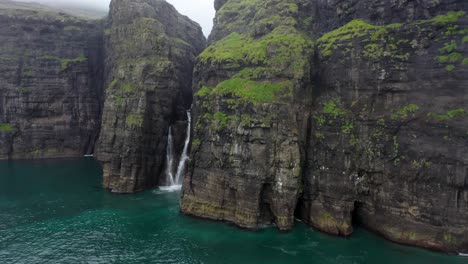 Revelación-Aérea-De-La-Cascada-Del-Acantilado-Del-Mar-De-La-Isla-Faroe,-Con-Aves-Marinas-Volando-Hacia-El-Dron