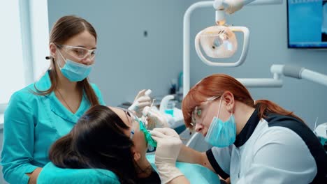 female patient visits stomatologist. dentist and assistant in mask and safety glasses treating client's tooth in dental cabinet. tooth treatment.