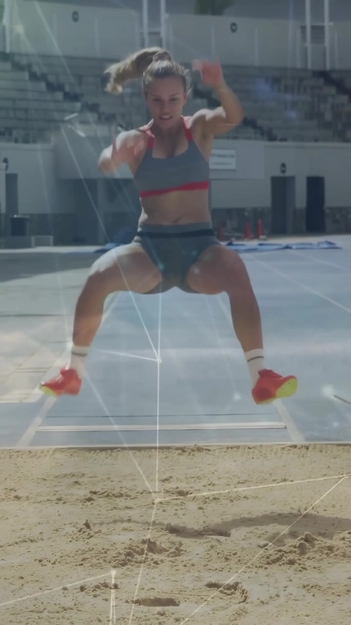 Video vertical: Atleta femenina en pista de atletismo, posicionándose en la tabla, despegando y aterrizando en la arena, con trazos de luz.