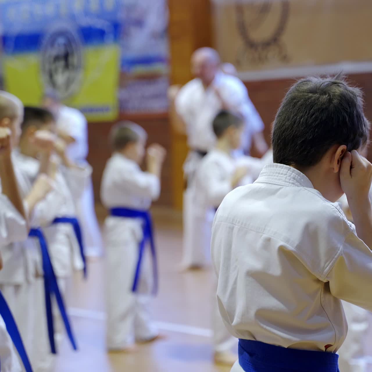 Athletes and their coaches in karate having training in a large gym. Kids in white kimonos make moves with hands. Blurred backdrop