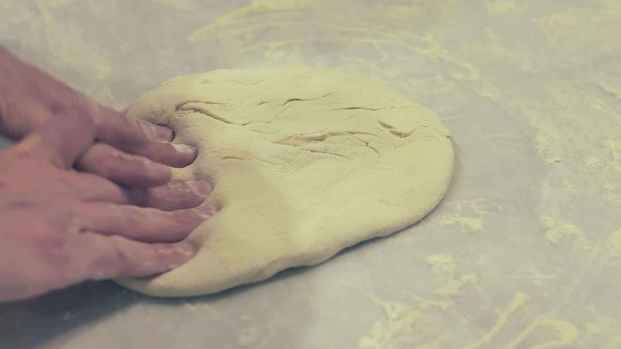 İtalyan bir aşçı, masanın üzerinde pizza hamurunu elleriyle çevirip geriyor.