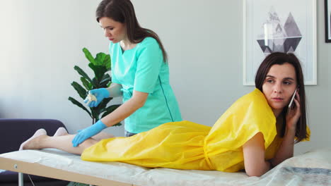 The-girl-talks-on-the-phone-and-smiles-during-hair-removal-on-her-legs.-Shugaring-master-removes-hair-from-legs