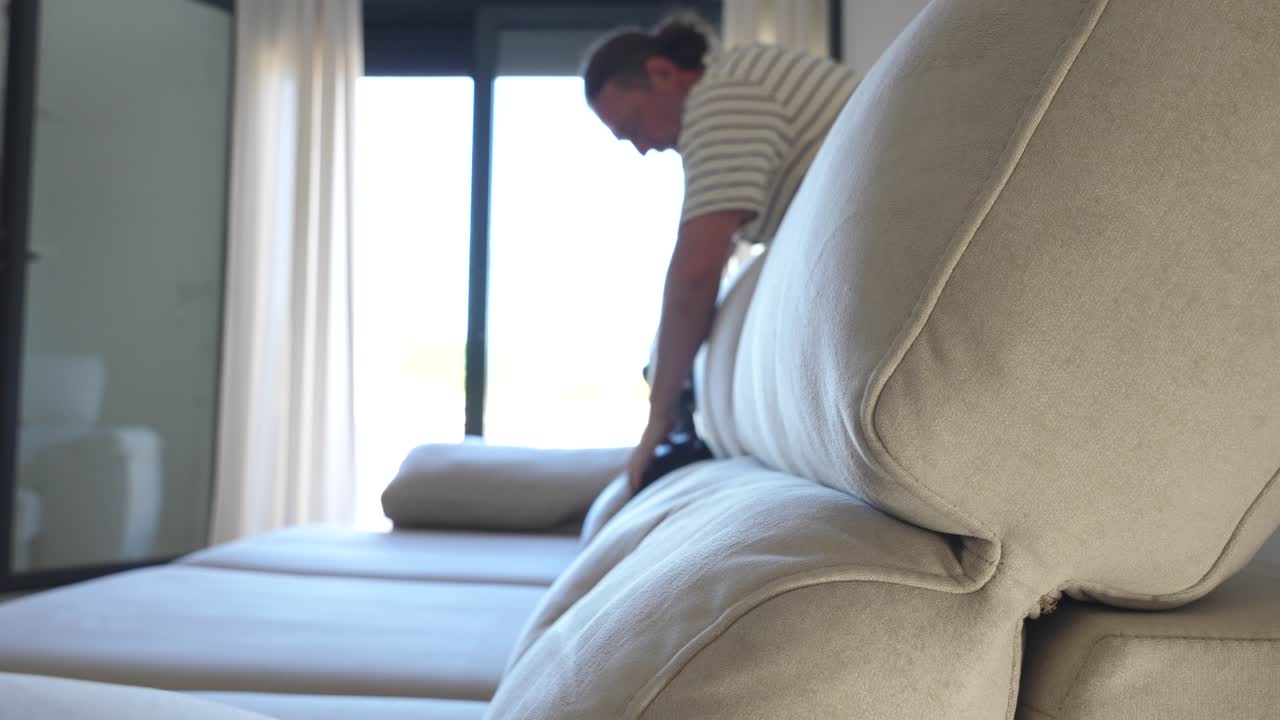 Grey sofa and man cleaning it in depth in the living room in background