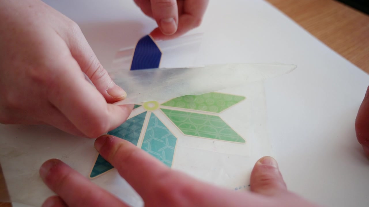 Manos colocando con cuidado un colorido diseño decorativo de vinilo en forma de flor sobre una lámina de transferencia transparente