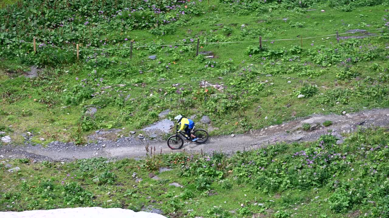 dos ciclistas van cuesta abajo en una pista sinuosa de tierra con casco y protecciones, alpes suizos, obwalden, vista aérea de drones
