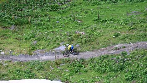 two bikers are riding downhill on a dirt sinuous track with helmet and protections, swiss alps, obwalden, drone aerial view