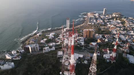 drone girar alrededor de la estación base de la torre de telecomunicaciones por encima del acantilado océano mar al atardecer con el horizonte de la ciudad
