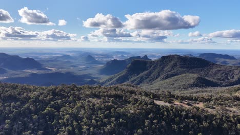 drone captures a sweeping panoramic view of forested mountains and valleys under scattered clouds in bright daylight, highlighting rugged australian wilderness