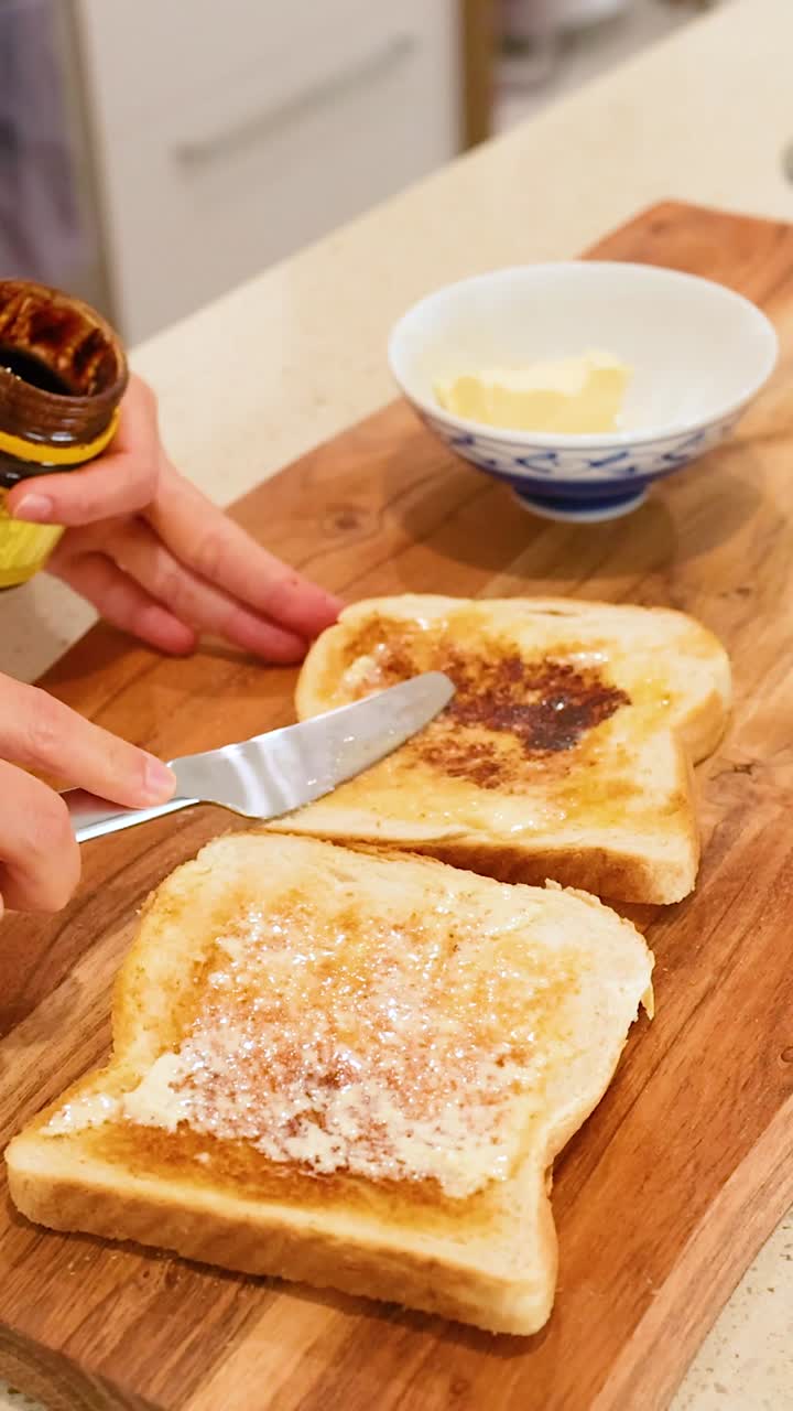 Close-up of hands spreading savory dark yeast extract onto buttered toast on a wooden board