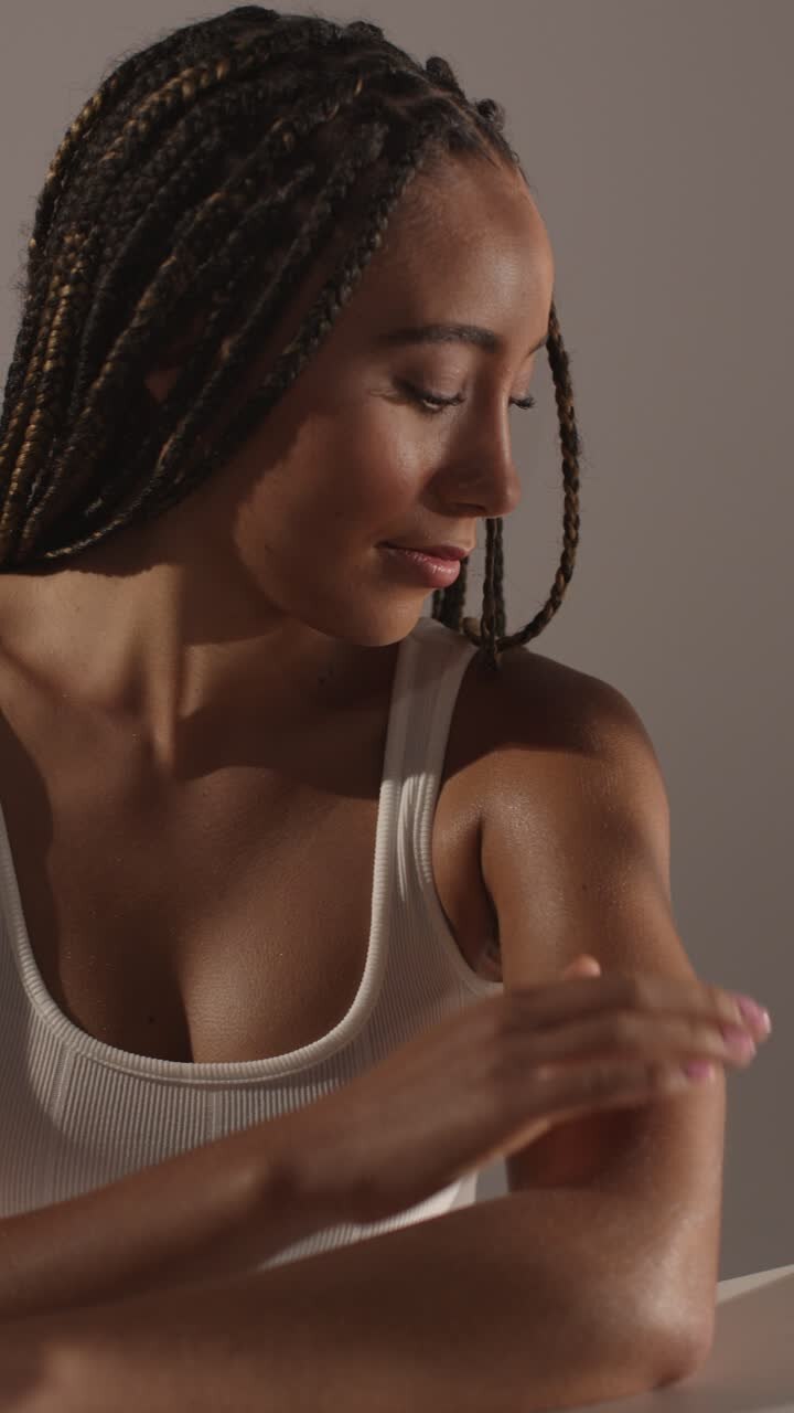 Studio Skincare Beauty Shot Of Young Woman With Long Braided Hair Putting Moisturiser Onto Arms