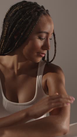 studio skincare beauty shot of young woman with long braided hair putting moisturiser onto arms