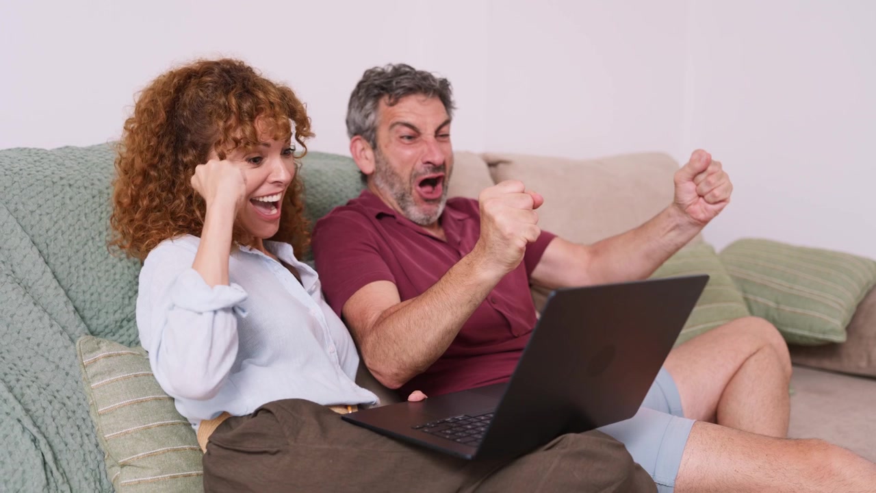 Coppia entusiasta che celebra il successo mentre usa il laptop sul divano