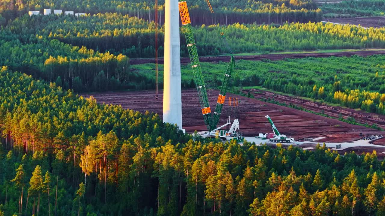 Crane assists in wind turbine base construction amid fields, early phase of installation, aerial medium orbit