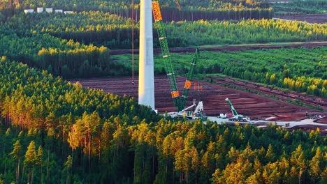 crane assists in wind turbine base construction amid fields, early phase of installation, aerial medium orbit