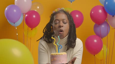 studio portrait of woman wearing birthday headband celebrating birthday blowing out candles on cake