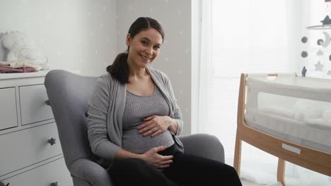 retrato de una mujer en estado avanzado de embarazo sentada en el sillón acariciándose el abdomen.