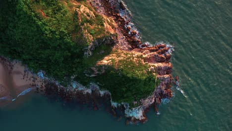 Aerial-rising-high-angle-view-above-lush-green-tropical-Lantau-island-hilltop-looking-down-over-ocean-waves-coastline