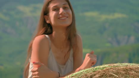 close up of a beautiful brunette womansmiling and laughing while leaning against a large bale of hay on a farm in france