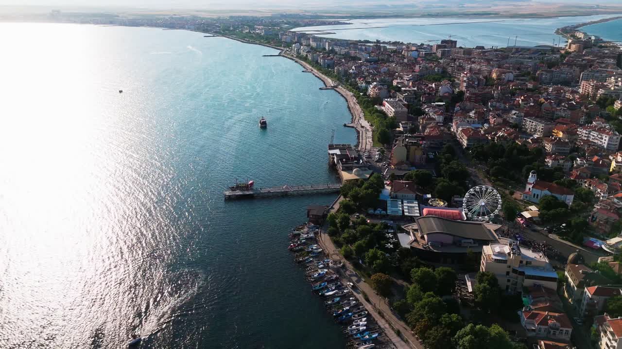Ripresa dall'alto con drone che mostra il molo, la costa, la ruota panoramica di Pomorie e la lontana terraferma con il sole che luccica sul mare.