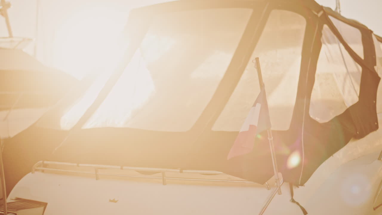 A French flag waves gently beside a sunlit boat canopy in a marina during early morning light