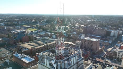 Bright-white-sunshine-during-aerial-orbit-around-cell-tower-on-top-of-American-city-building