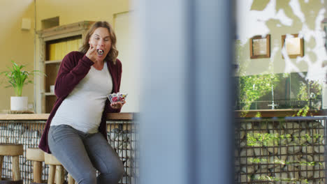 Caucasian-pregnant-woman-sitting-in-kitchen-and-eating-ice-cream