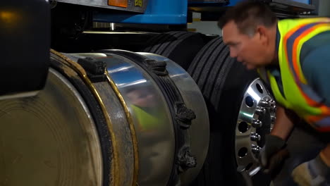man inspecting a semi-truck's tire and fuel tank