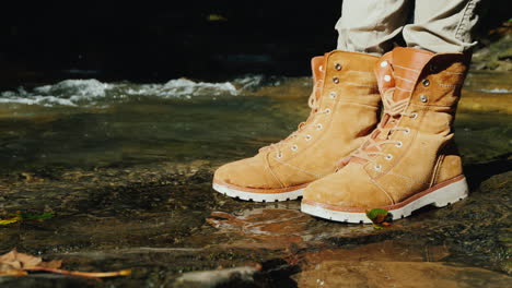 a tourist in trekking boots stands near a mountain stream hiking and active rest