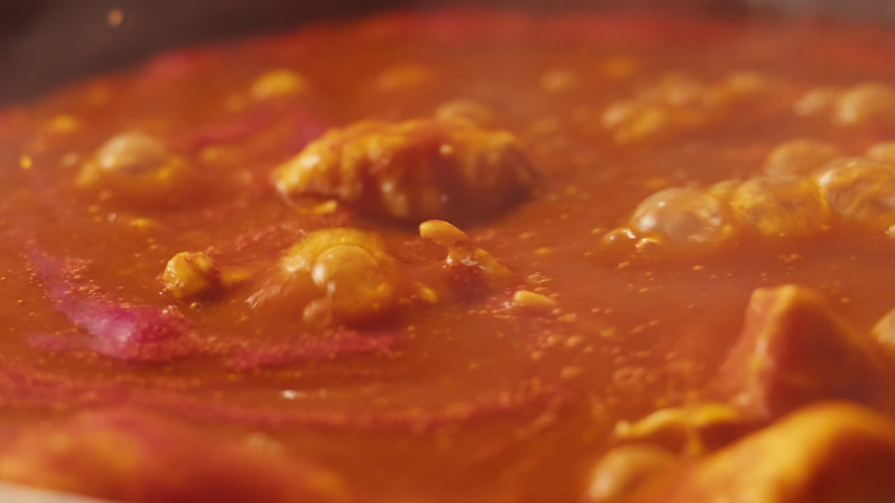 Chicken in tomato sauce is boiling on a frying pan with spices. Cooking tomato sauce curry with chicken fillet. Traditional Italian Mexican Asian dish. High quality studio shot for cafe, restaurant close up.