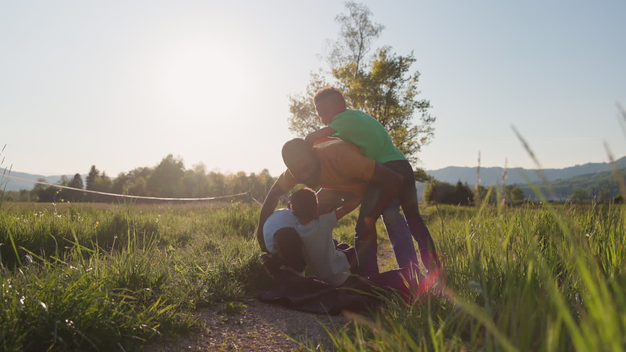 Un padre sonriente juega y lucha con sus hijos al aire libre en un día soleado, disfrutando de la diversión familiar en