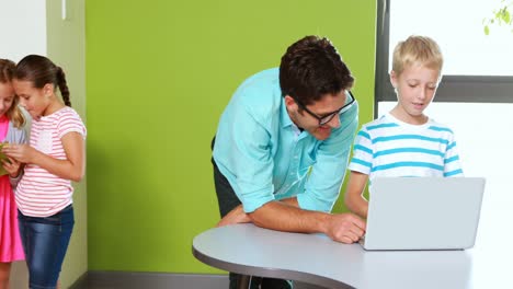 Teacher-and-schoolboy-using-laptop-in-classroom