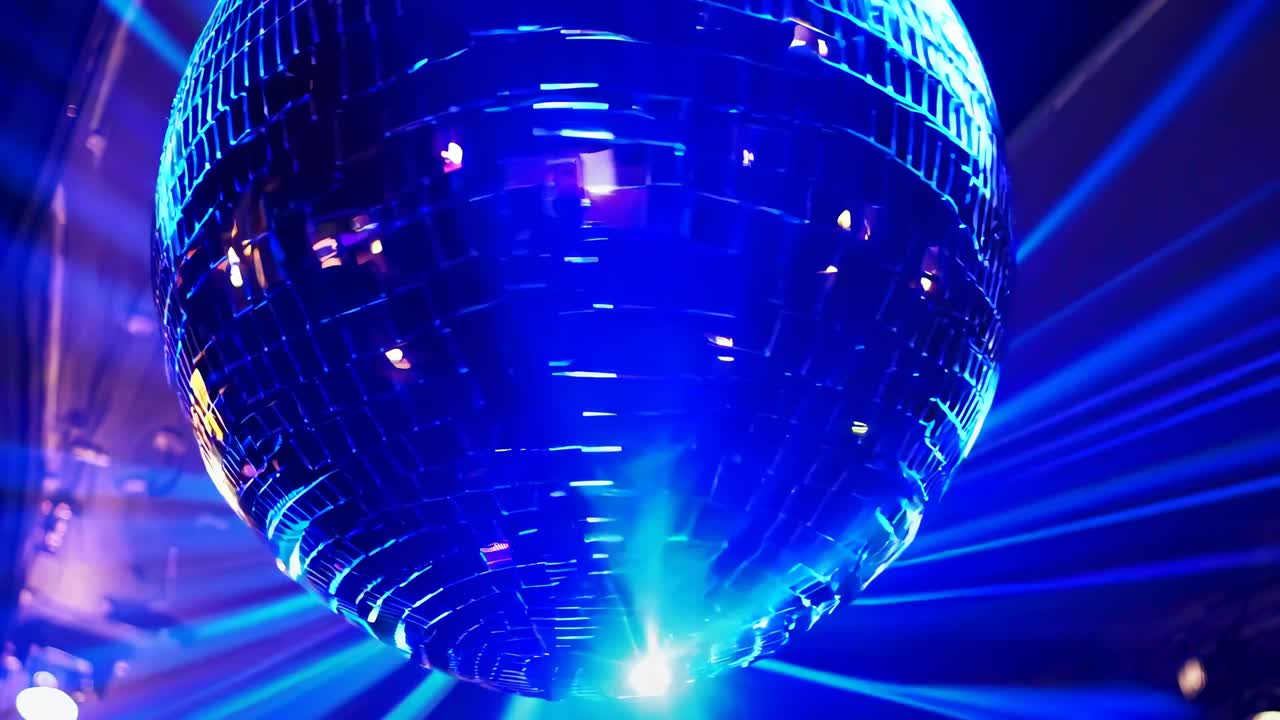 Primo piano, inquadratura dal basso di una palla da discoteca che riflette luci blu, creando un'atmosfera da festa vivace e retrò