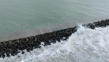 aerial establishing view of port of liepaja concrete pier , autumn storm, big waves splashing, overcast day, wide birdseye drone shot