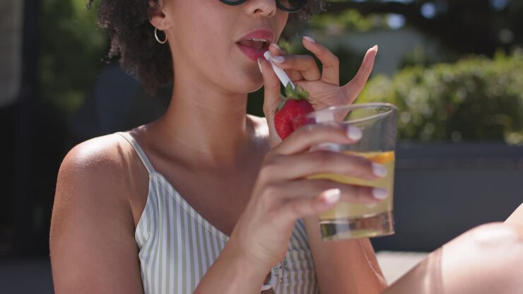 Woman's hand reaching from right is adjusting short glass on wooden deck lifting it for sipping