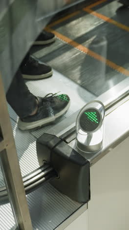 una vista en primer plano capturando una escalera mecánica en un centro comercial con personas que bajan. el enfoque está en los detalles mecánicos de la escalera y los reflejos de las personas en la superficie metálica