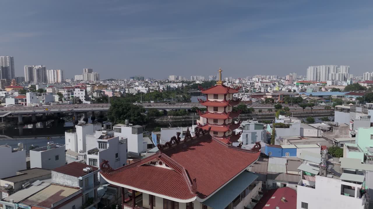 Panoramic drone view over Buddhist pagoda in busy urban area of Ho Chi Minh City, Vietnam on a sunny clear day featuring transportation infrastructure of main roads and canals in background
