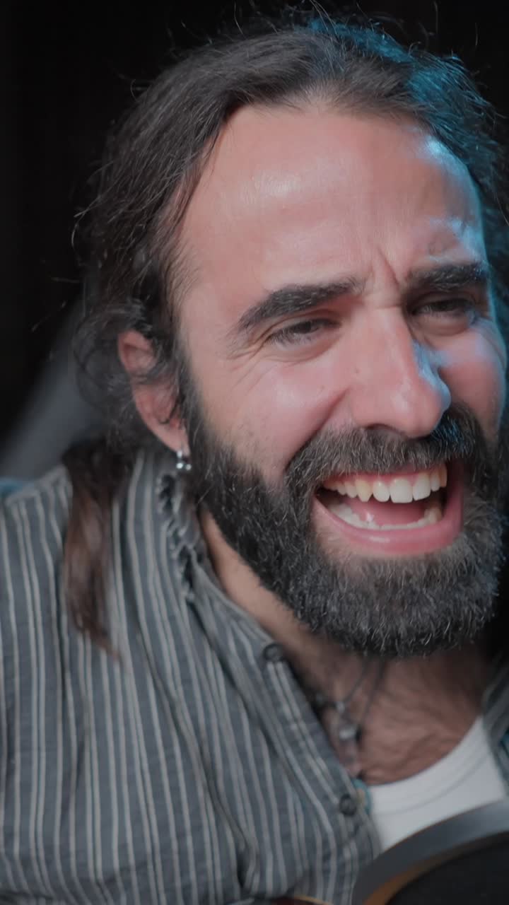 A man passionately singing and playing acoustic guitar into a microphone