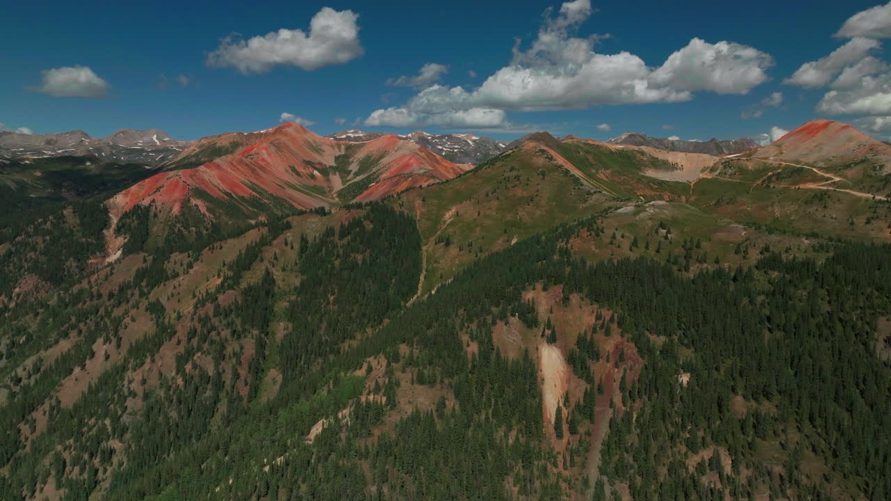 drone cinematográfico aéreo verano carretera de tierra de alta altitud silverton estación de esquí de montaña sur de colorado paso de montaña roja cielo azul tarde en la mañana impresionante verde exuberante cielo azul parcialmente nublado montañas rocosas